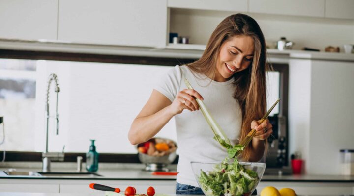Mujer joven preparando una ensalada en casa como parte de una alimentación saludable y equilibrada.
